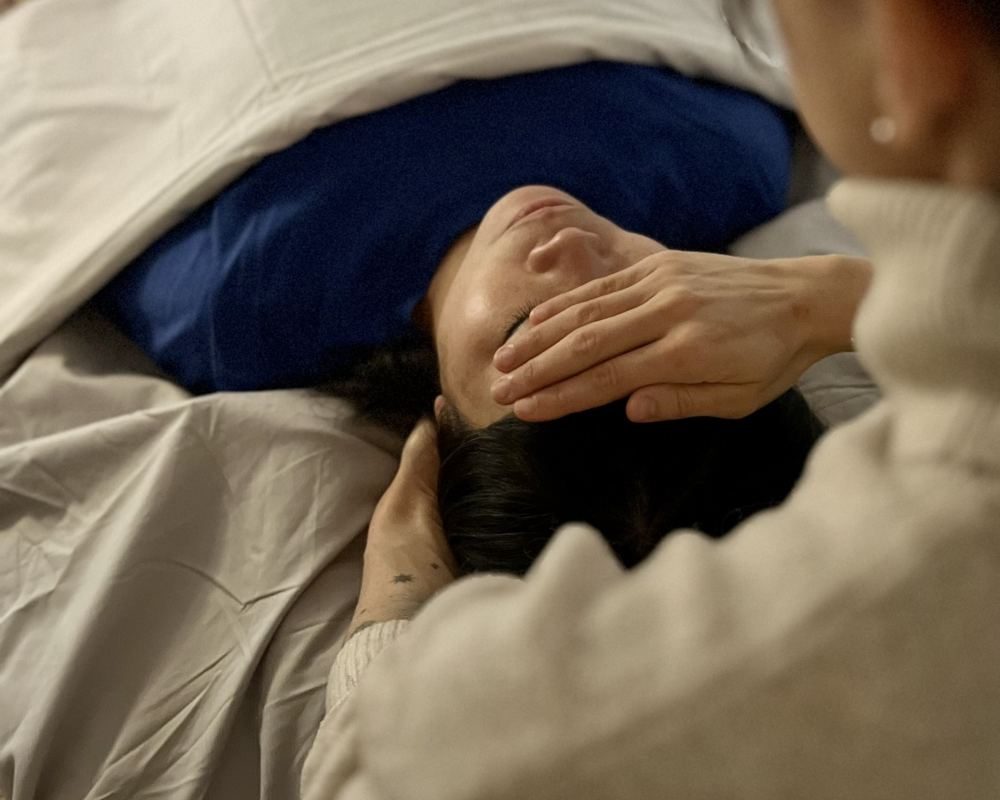 A therapist's hands resting lightly on a client's forehead and head during an oncology massage session